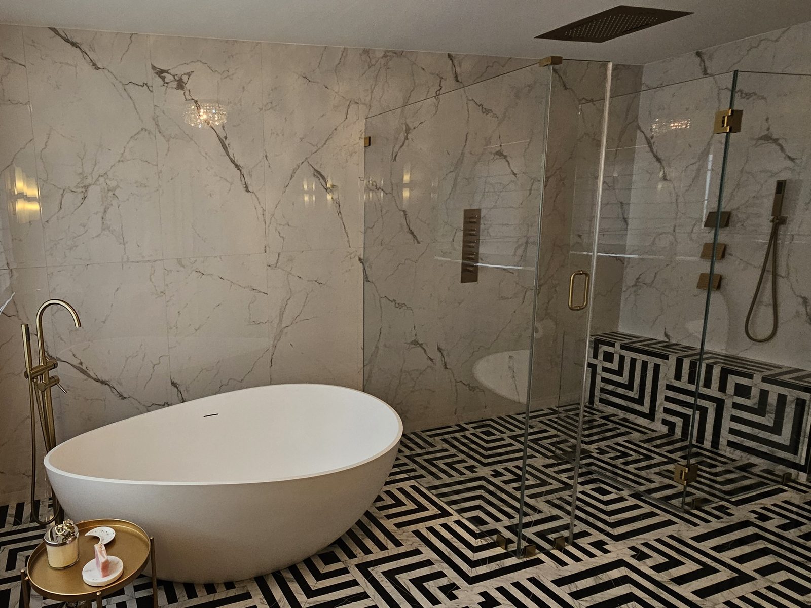 Marble primary bath with freestanding tub and graphic black and white floor